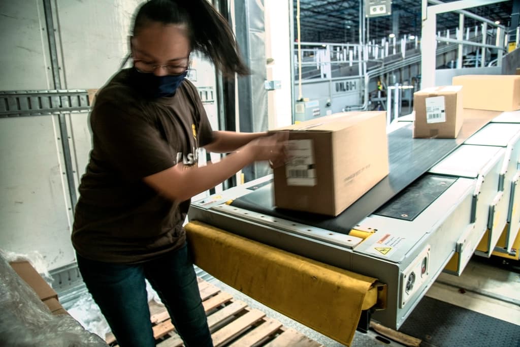 A warehouse worker packing an online order into a cardboard box on a conveyor